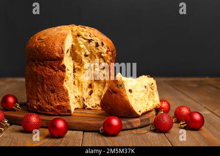 Board with cut Panettone and Christmas balls on table against black background Stock Photo