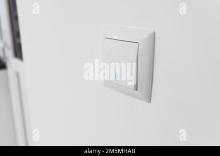 Light switch. White plastic mechanical switch installed on a white wall. Turn on and off. White light power switch. Stock Photo