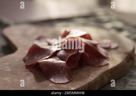 Dried pastrami slices on a wooden board with natural light, shallow focus Stock Photo