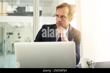 Hes got big plans for his business. a businessman looking thoughtful while using his laptop. Stock Photo