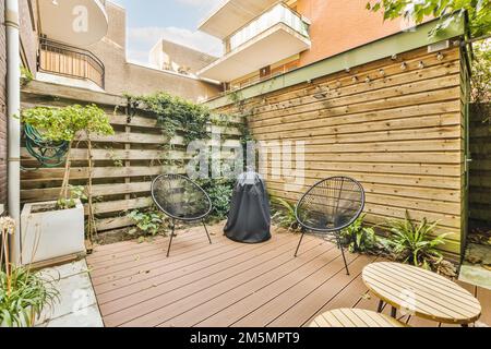 a backyard area with wooden decking and plants on the wall, two chairs and a table in the corner Stock Photo