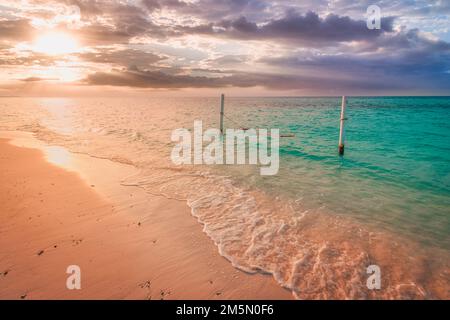 Tranquil summer vacation or holiday landscape. Tropical sunset beach view, sand sky with sea water waves, over water hammock. Calm exotic nature scene Stock Photo