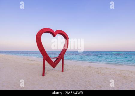 Wooden heart shape beach decoration. Sunset pastel colors twilight sky, sandy shore, seascape horizon. Romantic Valentines day, honeymoon romance Stock Photo