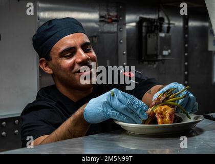 ARABIAN GULF (March 29, 2022) Culinary Specialist 3rd Class Josiah Gonsalves prepares a dinner plate to be served during a March birthday month celebration aboard the guided-missile destroyer USS Gridley (DDG 101) in the Arabian Gulf, March 29. Gridley is deployed to the U.S. 5th Fleet area of operations to help ensure maritime security and stability in the Middle East Region. Stock Photo