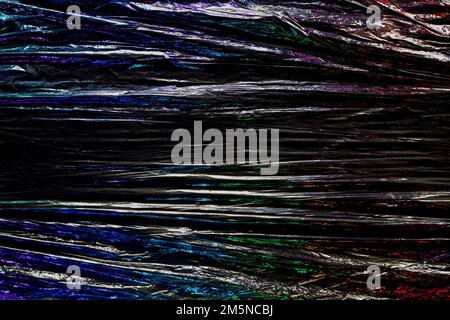 Black color plastic wrap background. Dark crumpled wrinkled plastic cellophane. Reflecting colorful iridescent light and shadow on creases and folds Stock Photo