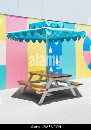 A picnic table with a blue umbrella and a multicolored pastel background . Stock Photo