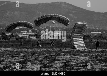 In preparation for Exercise Orion, Greek Special Operations Forces (SOF) members land at the drop zone near Elefsina, Greece during airborne operation while a U.S. SOF Soldier observes after gathering his parachute, March 29, 2022. Exercise Orion reinforces Greece as a regional SOF leader, enhances interoperability across multiple domains, and strengthens relationships with NATO and non-NATO partners. The exercise focuses on highlighting operational capabilities, international collaborations and conventional and hybrid warfare training. Stock Photo