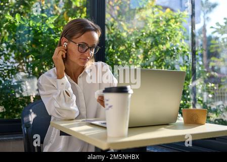 Cheerful mature businesswoman working from cafe, having online video call using laptop.  Stock Photo