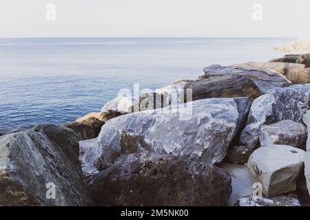 Close up of big stones of mediterranean sea shoe. Stone wave breakers of Italian coast on a sunny summer day. Genoa, region of Liguria, Italy.  Flat s Stock Photo