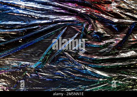 Black color plastic wrap background. Dark crumpled wrinkled plastic cellophane. Reflecting colorful iridescent light and shadow on creases and folds Stock Photo