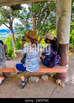 Khao Tut, Phuket, Thailand, Group Chinese Tourists,  People Visiting Tropical Island, 'Big Buddha', Woman from behind sitting on Bench Photographing Landscape with Smart Phones, Diverse travellers Stock Photo