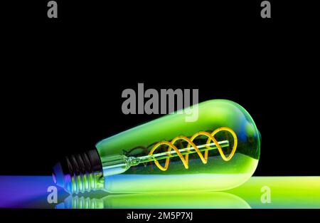 Colourful patterns reflect within a clear glass, oval shaped lightbulb and photographed against a black background Stock Photo