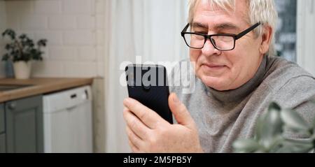 Hoary old man looking at web camera, holding phone, talking with children, wife online. Senior grandpa smiling chatting with friends, family via video Stock Photo