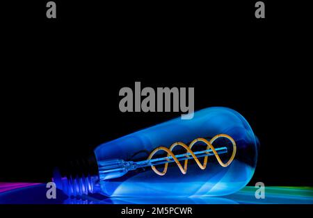 Colourful patterns reflect within a clear glass, oval shaped lightbulb and photographed against a black background Stock Photo