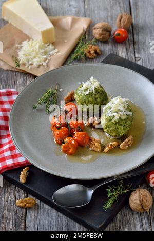 South Tyrolean spinach dumplings served with browned butter, baked cherry tomatoes, walnuts and grated parmesan cheese Stock Photo
