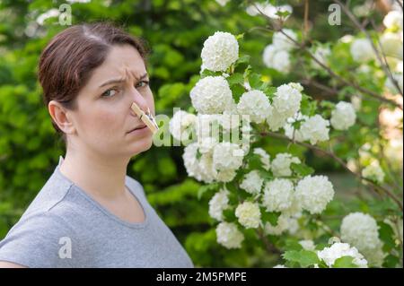 Unhappy woman with a clothespin on her nose on a walk in a blooming park.  Stock Photo