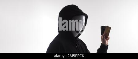 Hacker man and credit cards in hand. Represent credit cards personal data stolen by anonymous man in Black hood shirt. Credit cards data security and Stock Photo
