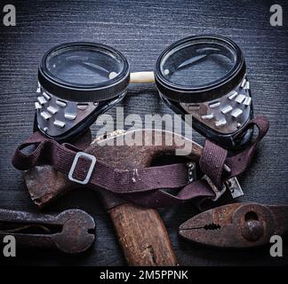 goggles hammer pliers on vintage wood board. Stock Photo