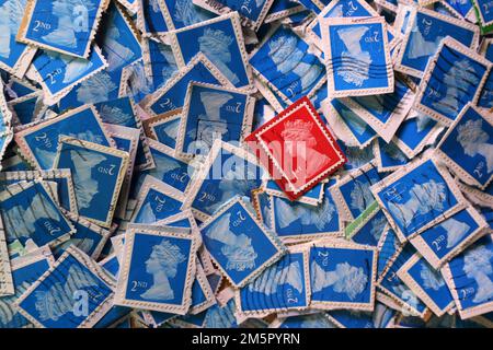 Used UK franked postage stamps being collectd for a charity contribution. A colourful selection of use British Royal Mail postage stamps in close up. UK Britain. Red First Class (1st) stamp on a background of Blue Second (2nd) Class stamps Stock Photo