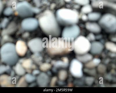 Blur photo or defocused abstract background of smooth small rocks on black sand. For wallpapers Stock Photo