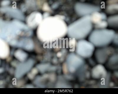 Blur photo or defocused abstract background of smooth small rocks on black sand. For wallpapers Stock Photo