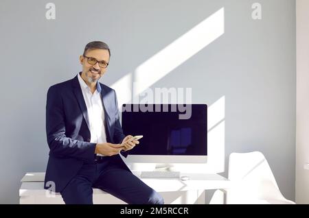 Successful and confident middle-aged business man who posing with modern smartphone in his hands. Stock Photo