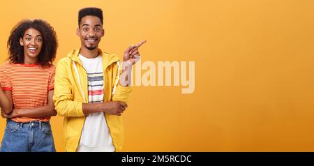 Which one telling true. Joyful and friendly good-looking couple, african american woman pointing left and dark-skinned guy right smiling broadly at Stock Photo