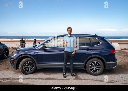 Portrait of mid adult man with coffee standing by blue car at beach Stock Photo