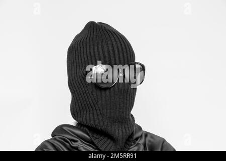 Hat balaclava on a girl and sunglasses on a white background, the face of a thief in a hat with a slit for verbs Stock Photo