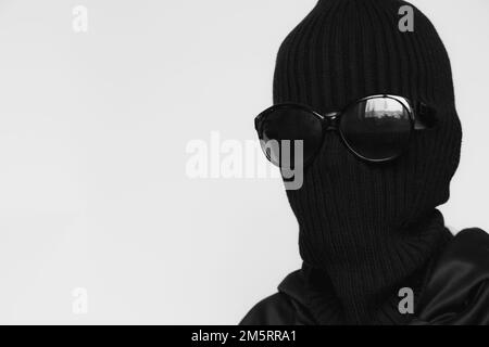 Hat balaclava on a girl and sunglasses on a white background, the face of a thief in a hat with a slit for verbs Stock Photo