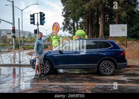 Man showing google android statues in garden standing by car on wet street Stock Photo
