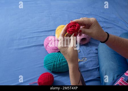 Goiania, Goiás, Brazil – December 30, 2022: A woman sitting on a bed with spools of colored thread around her and a detail of a hand holding a rose. Stock Photo