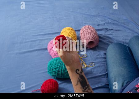 Goiania, Goiás, Brazil – December 30, 2022: A woman sitting on a bed with spools of colored thread around her and a detail of a hand holding a rose. Stock Photo