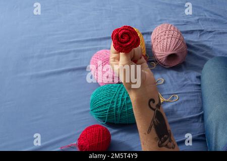 Goiania, Goiás, Brazil – December 30, 2022: A woman sitting on a bed with spools of colored thread around her and a detail of a hand holding a rose. Stock Photo