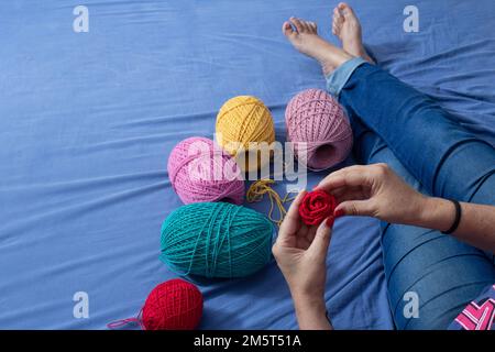 Goiania, Goiás, Brazil – December 30, 2022: A woman sitting on a bed with spools of colored thread around her and a detail of a hand holding a rose. Stock Photo