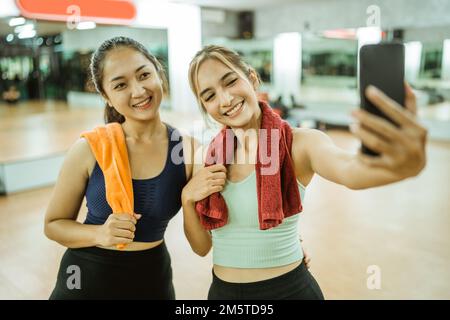 two sporty women smiling while taking selfie together using smartphone Stock Photo