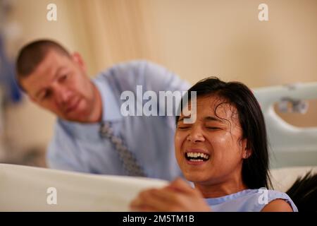 It always seems impossible until its done. a young woman giving birth with her husband supporting her in the background. Stock Photo