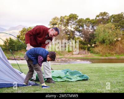 There you go. a father and son setting up a tent together while camping. Stock Photo