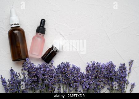 Flat lay composition with lavender flowers and natural essential oil bottles on white concrete background. Copy space Stock Photo