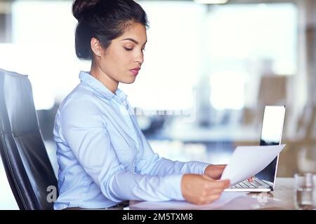 One of those busy days at the office...a young businesswoman going over paperwork at her desk. Stock Photo
