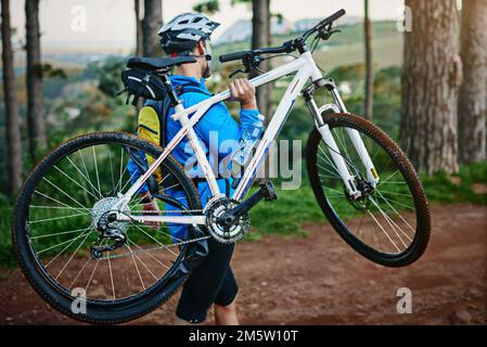 Taking his bike out for a spin. a male cyclist walking along a trail carrying his mountain bike. Stock Photo