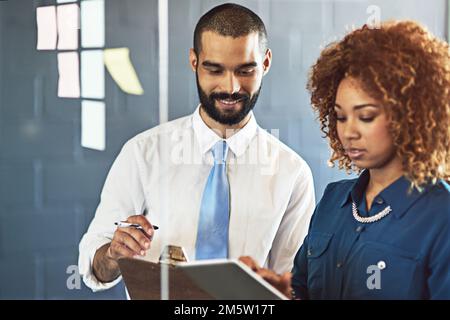Developing new strategies as a team. two young professionals brainstorming with sticky notes on a glass wall in an office. Stock Photo