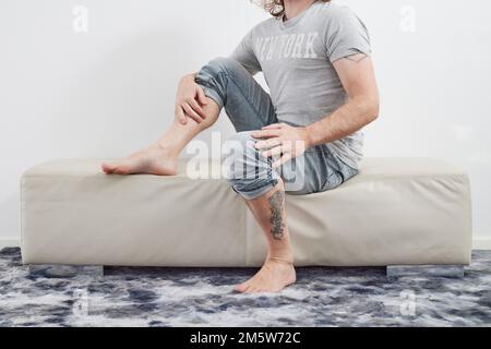 Man sitting barefoot on couch Stock Photo