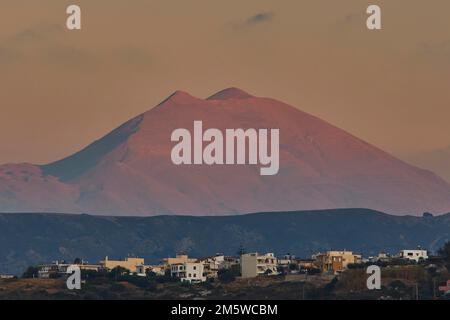 Red evening light, houses on hill, Ida massif, double peak, close, Psiloritis, light blue sky, few grey clouds, Rethimnon, central Crete, island of Stock Photo