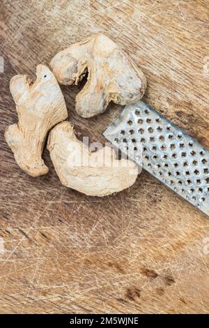 Dried ginger root pieces and metal grater on a rustic wooden surface. Spice ingredient prep. Stock Photo