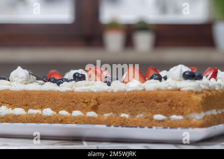 Close-up of a delicious cake with cream, strawberries, and blueberries. Appetizing dessert texture. Stock Photo