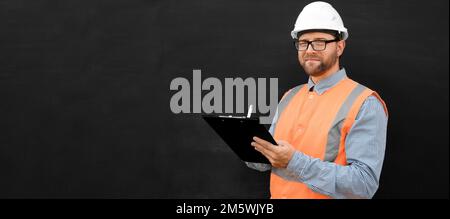 Male Engineer in a White Hard Hats and Orange West. Handsome Confident Build Worker Isolated on Blank Black Background. Copy Space. He Work in a Heavy Stock Photo