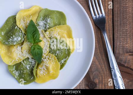 Plate of delicious green and yellow ravioli with cheese and basil on rustic wooden table. Italian food. Stock Photo