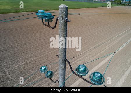 Aerial view of a power line pole with glass insulators over cultivated field. Infrastructure and agriculture. Stock Photo
