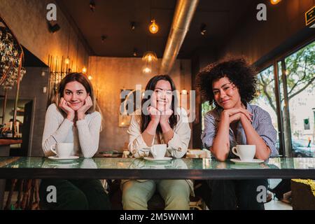 Portrait of thee young women smiling and posing looking at camera on a coffee shop. Photo of a group of happy females on a restaurant or bar. High quality photo Stock Photo